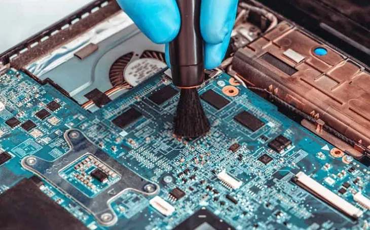 Nhân viên kỹ thuật đang thực hiện thao tác vệ sinh laptop, bao gồm cả các khe tản nhiệt